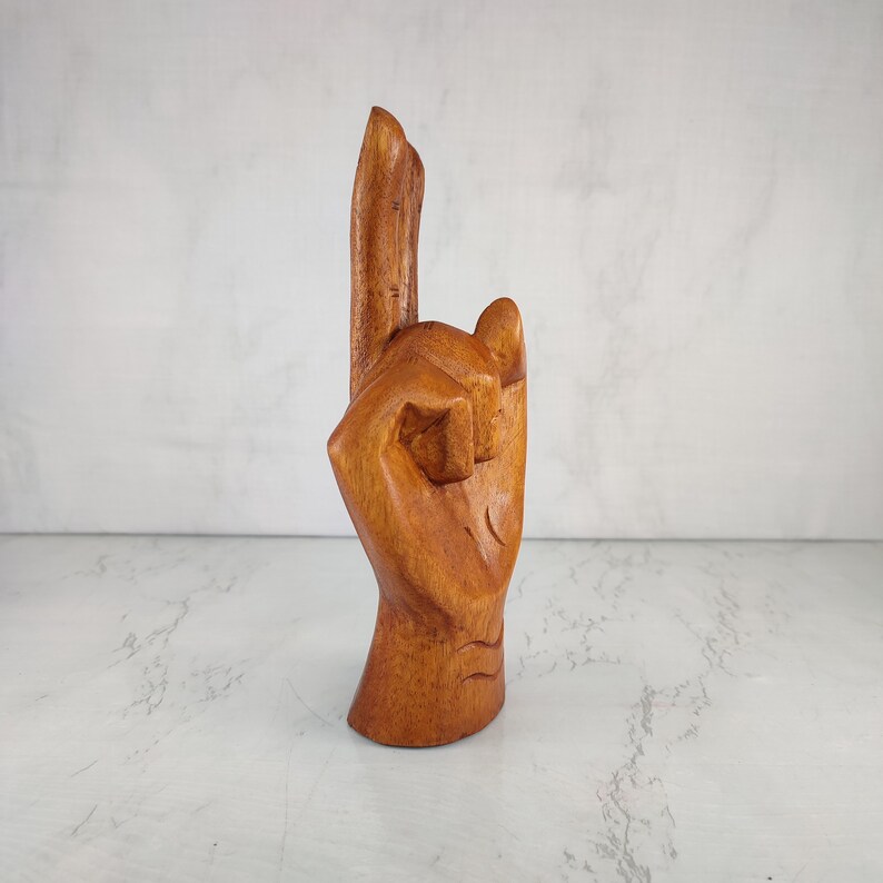 May include: A wooden hand sculpture with the index finger pointing up, carved in a light brown color.