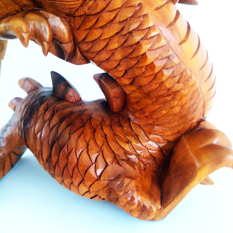 May include: A wooden carving of a dragon with intricate scales, the dragon is curled up with its tail in its mouth.
