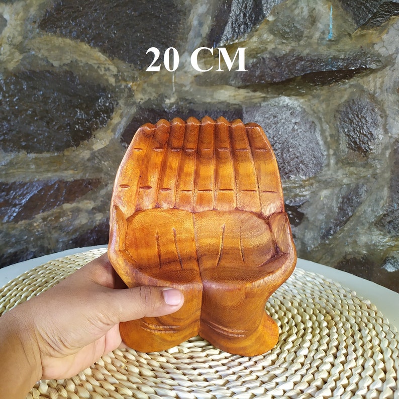 Pu&ograve; includere: Una scultura in legno di due mani giunte, scolpite in un colore marrone chiaro. La scultura &egrave; alta 20 cm e ha una finitura liscia e lucida.