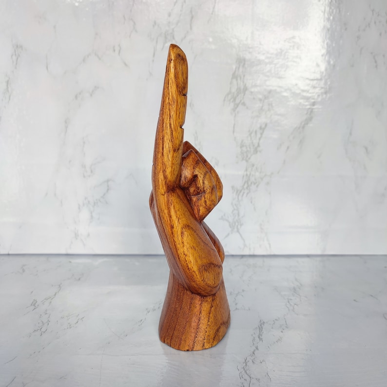 May include: A wooden hand sculpture with the index finger pointing up. The hand is carved from a light brown wood and has a natural finish.
