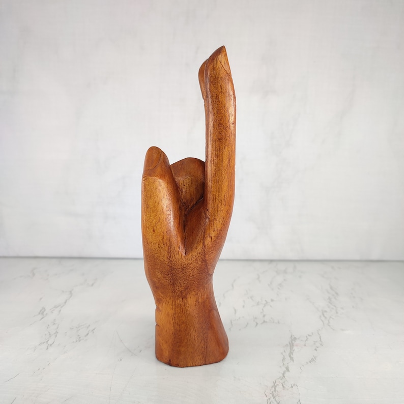 May include: A wooden hand sculpture with the index finger pointing up. The hand is carved from a light brown wood and has a smooth finish.