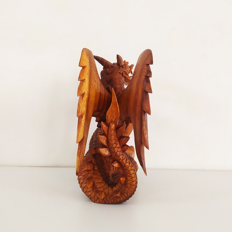 May include: A wooden dragon sculpture with intricate details, carved from a single piece of wood. The dragon is depicted with outstretched wings and a curled tail.