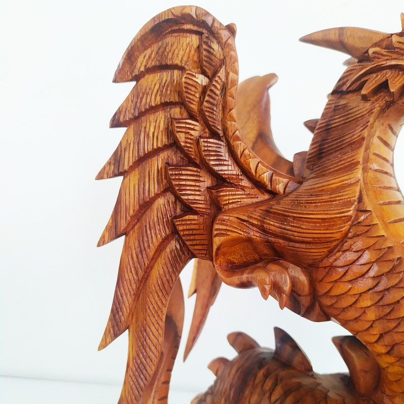 May include: A wooden carving of a dragon with intricate details. The dragon has large wings and a long tail. The carving is made of light brown wood.