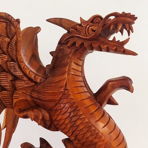 May include: A detailed wooden carving of a dragon with wings outstretched. The dragon is made of reddish-brown wood and has a fierce expression.