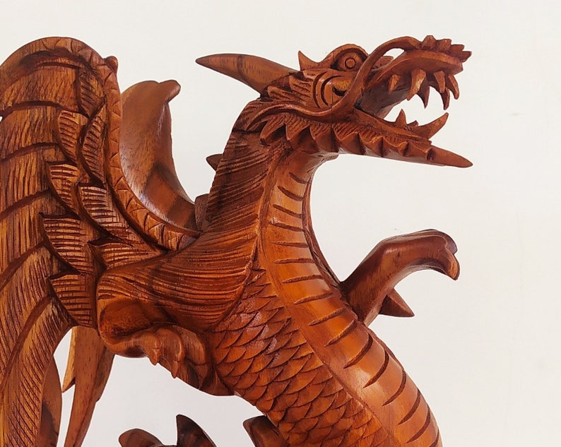 May include: A detailed wooden carving of a dragon with wings outstretched. The dragon is made of reddish-brown wood and has a fierce expression.