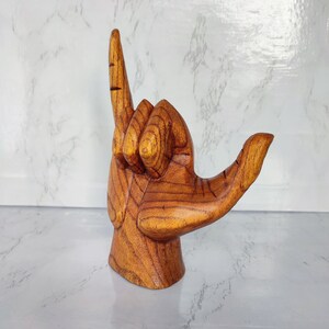 May include: A wooden hand sculpture in a 'shaka' gesture, a popular Hawaiian greeting. The hand is carved from light brown wood with a natural grain pattern.