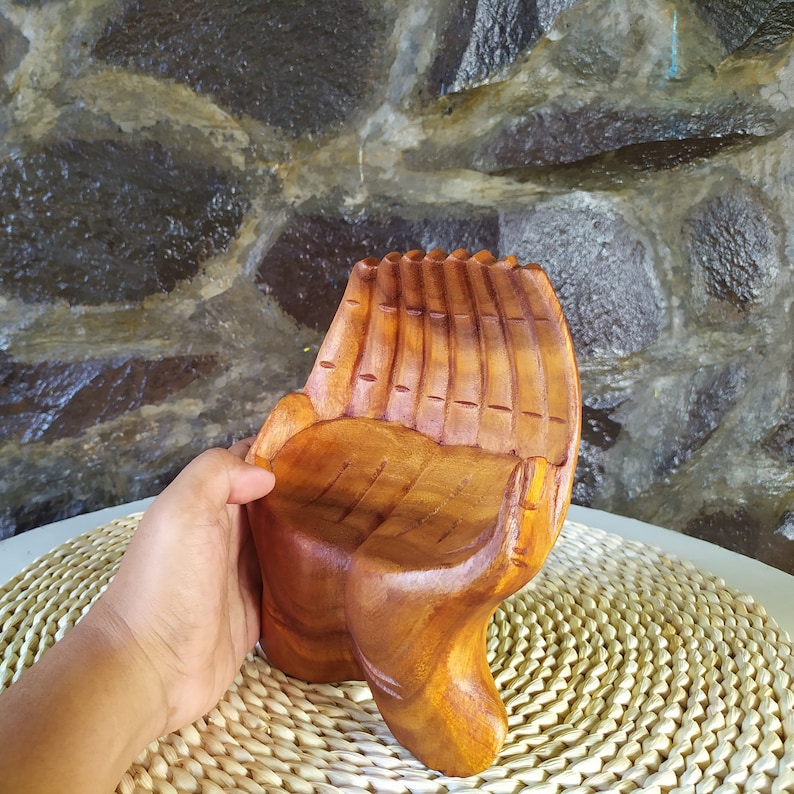 Pu&ograve; includere: Una scultura di mano in legno con un centro cavo, perfetta per contenere piccoli oggetti. La scultura &egrave; realizzata in legno marrone chiaro e ha una finitura naturale e rustica.