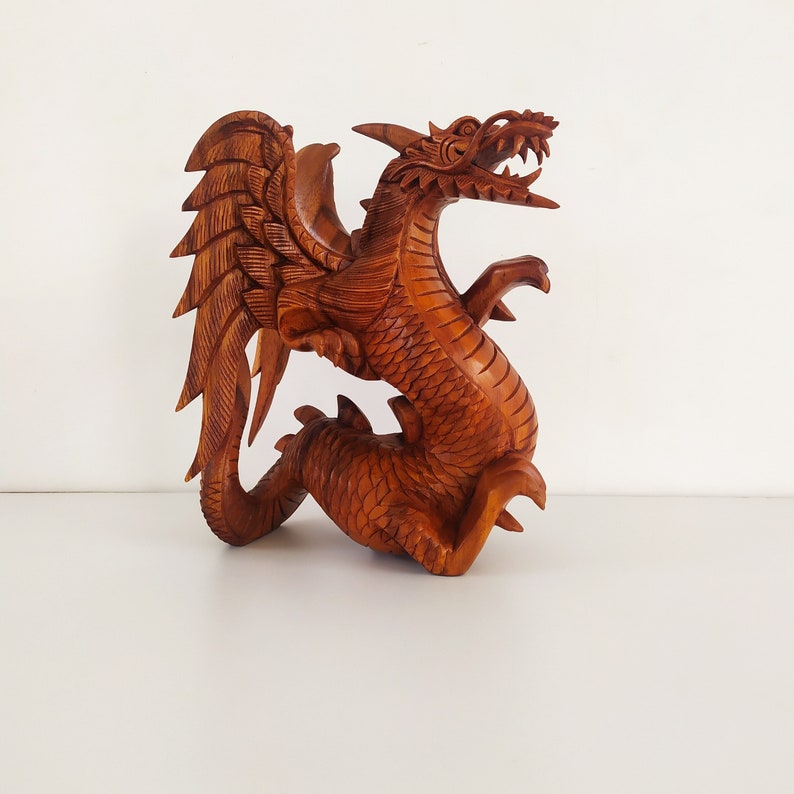 May include: A hand-carved wooden dragon sculpture with intricate details. The dragon is brown and has wings, a long tail, and a fierce expression.