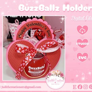 Puede incluir: Un portaregalos en forma de corazón para el Día de San Valentín, con una combinación de colores rojo y rosa. El soporte presenta una cinta con patrones de corazones y contiene un enfriador BuzzBallz Strawberry. El diseño incluye el texto "Happy Valentine's Day".