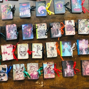 Puede incluir: Una colección de 30 pequeños cuadernos hechos a mano con varios diseños. Los cuadernos están decorados con cintas de colores y presentan temas como Halloween, fantasía y cultura pop.