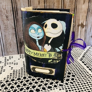 Può includere: Un diario fatto a mano con una copertina con Sally e Jack Skellington di Nightmare Before Christmas. La copertina è blu scuro con le parole "SIMPLY MEANT TO BE". Un nastro viola è legato attorno al diario.