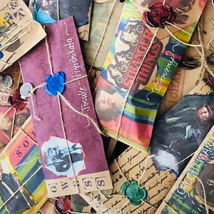 May include: A collection of rectangular paper envelopes featuring various printed graphics, including character portraits, floral patterns, and the text Stranger Things. Each envelope is tied with twine and sealed with a coloured wax seal.