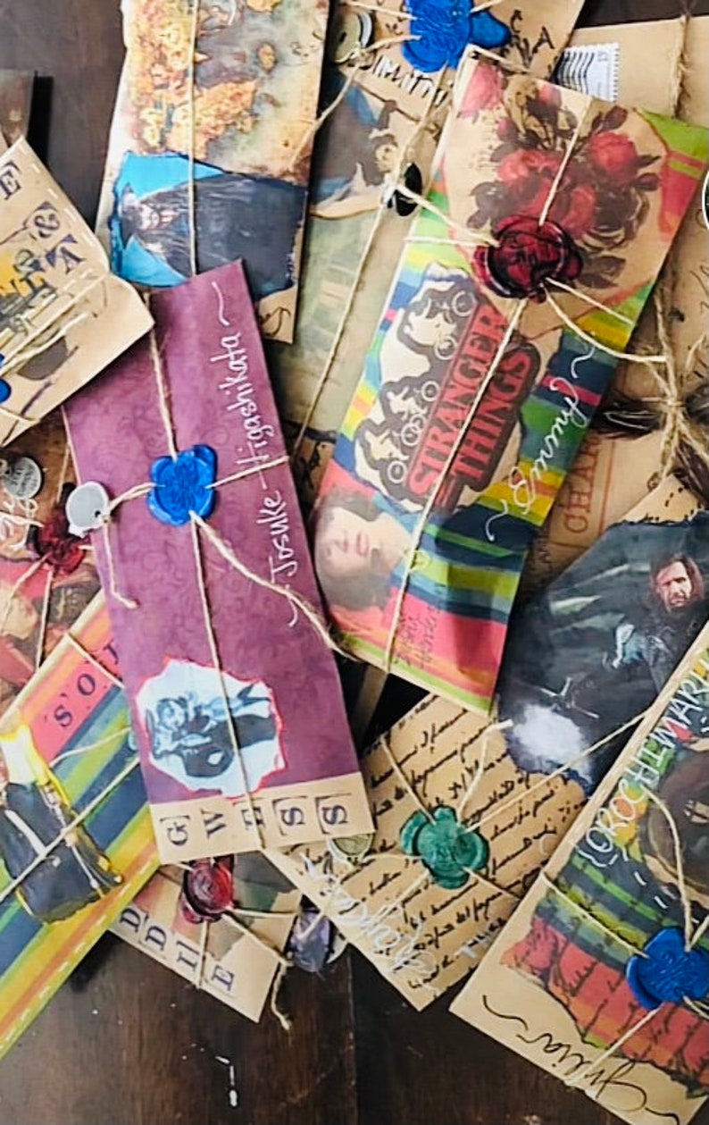 May include: A collection of rectangular paper envelopes featuring various printed graphics, including character portraits, floral patterns, and the text Stranger Things. Each envelope is tied with twine and sealed with a coloured wax seal.