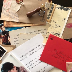 May include: A collection of assorted stationery items including handwritten letters, envelopes, a wooden wax seal stamp, and printed photographs. One red envelope features cursive handwriting and a postage stamp, while other papers display text.