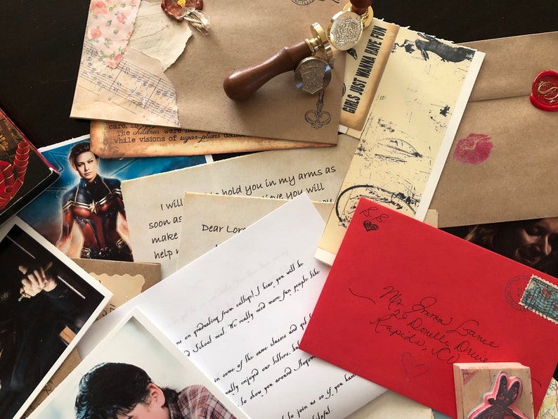 May include: A collection of assorted stationery items including handwritten letters, envelopes, a wooden wax seal stamp, and printed photographs. One red envelope features cursive handwriting and a postage stamp, while other papers display text.