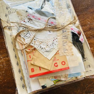 May include: A clear plastic bag filled with various vintage paper ephemera, including lace, music sheets, and a bingo card. The bag is tied with twine and labelled "FAITH".