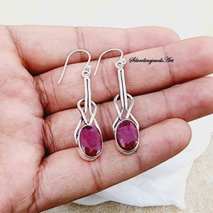 May include: A pair of silver dangle earrings with a red ruby gemstone in each. The earrings feature a delicate, twisted design.