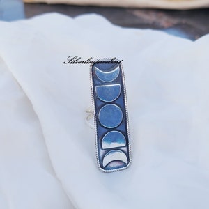 Könnte beinhalten: Ein silberner Ring mit einem rechteckigen Design, das eine Reihe von Mondphasen zeigt. Der Ring ist aus Sterlingsilber gefertigt und hat eine polierte Oberfläche.