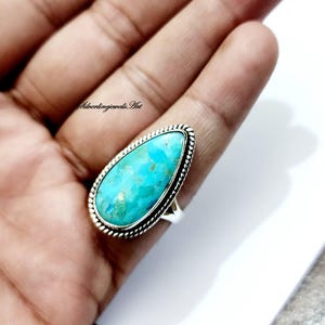 May include: A turquoise gemstone ring with a teardrop-shaped stone set in a silver band with a braided edge.