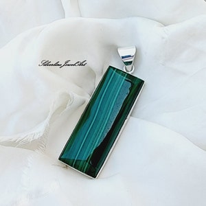 Puede incluir: Un colgante de plata con una piedra rectangular de malaquita verde. La piedra tiene un patrón estriado y está engastada en un marco de plata.