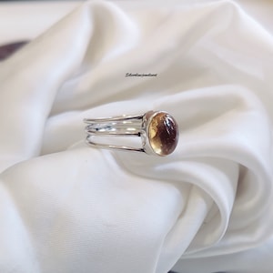May include: A silver ring with a three-band design and a round, light brown gemstone.
