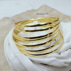 May include: A set of six gold-toned bangle bracelets stacked on top of each other. The bracelets are smooth and shiny.