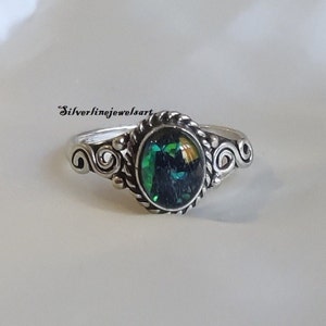Puede incluir: Un anillo de plata con una piedra preciosa verde engastada en un bisel decorativo. La banda presenta un diseño de cuerda trenzada y volutas.