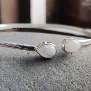Puede incluir: Un brazalete de plata con dos acentos de piedra lunar en forma de lágrima.