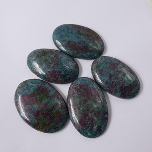 May include: Five oval-shaped gemstones with a polished finish. The stones feature a mix of teal, green, and maroon colors. The gemstones are arranged on a white surface.