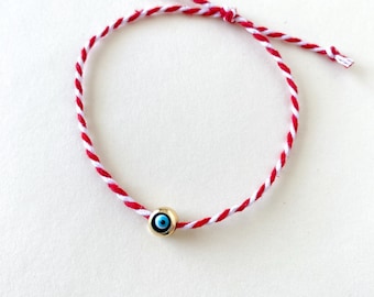 Könnte beinhalten: Rotes und weißes Armband aus Schnur mit einem goldenen bösen Blick-Anhänger.