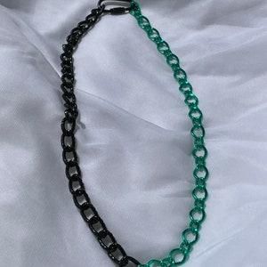 May include: A black and green chain necklace with a clasp. The chain is made of two different colors, with one half being black and the other half being green.