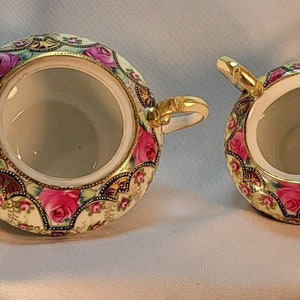 May include: A vintage porcelain sugar and creamer set with a floral design. The set features a gold trim and pink roses on a cream background.