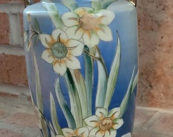 May include: A blue and white porcelain vase with gold accents and floral designs. The vase has two handles and a flared base.
