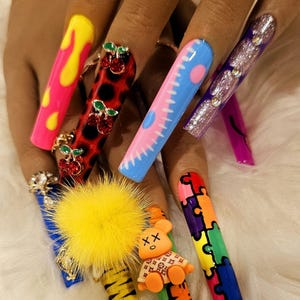May include: Long, colorful, and decorated acrylic nails with various designs, including cherries, a teddy bear, a puzzle, and a yellow pom-pom.
