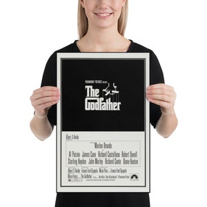 May include: A black and white poster for the movie "The Godfather" featuring the film's title and a silhouette of a hand holding strings with puppets. The poster also includes the names of the actors and director.