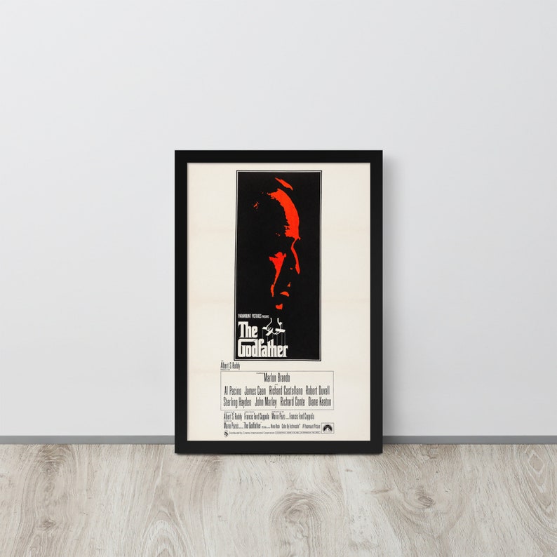 May include: A black and white movie poster for the film "The Godfather" featuring a close-up of Marlon Brando's face in red. The poster includes the film's title, director, and cast.