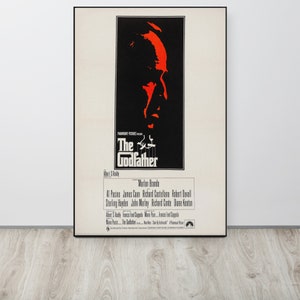 May include: A vintage movie poster for the film "The Godfather" featuring a red silhouette of Marlon Brando's face. The poster also includes the film's title, director, and cast.