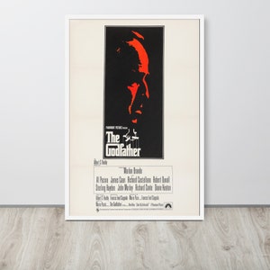 May include: A vintage movie poster for the film "The Godfather" featuring a close-up of Marlon Brando's face in red and black. The poster also includes the film's title, director, and cast.