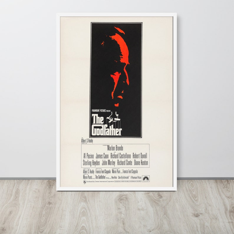 May include: A vintage movie poster for the film "The Godfather" featuring a close-up of Marlon Brando's face in red and black. The poster also includes the film's title, director, and cast.