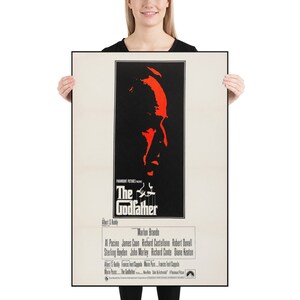 May include: A vintage movie poster for the film "The Godfather" featuring a red silhouette of Marlon Brando's face against a black background. The poster includes the film's title, director, and cast.