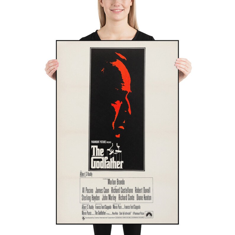 May include: A vintage movie poster for the film "The Godfather" featuring a red silhouette of Marlon Brando's face against a black background. The poster includes the film's title, director, and cast.