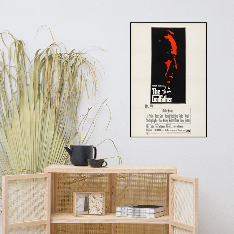 May include: A vintage movie poster for the film "The Godfather" featuring a black and white image of Marlon Brando's face. The title of the film is in red and white text.