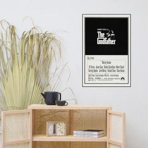 May include: A black and white movie poster for the film "The Godfather" featuring the title in a bold white font. The poster also includes the names of the actors, including Marlon Brando, Al Pacino, James Caan, and Robert Duvall.