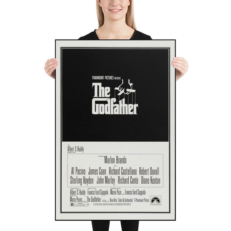 May include: A black and white poster for the movie "The Godfather" featuring the title in a stylized font with a hand holding a puppet. The poster also includes the names of the actors, director, and producer.