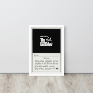 May include: A black and white movie poster for the film "The Godfather" featuring the title in large white letters and the names of the actors in smaller white letters. The poster also includes the Paramount Pictures logo.