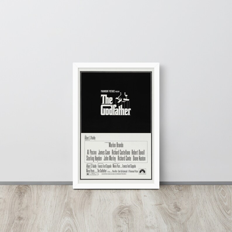 May include: A black and white movie poster for the film "The Godfather" featuring the title in large white letters and the names of the actors in smaller white letters. The poster also includes the Paramount Pictures logo.