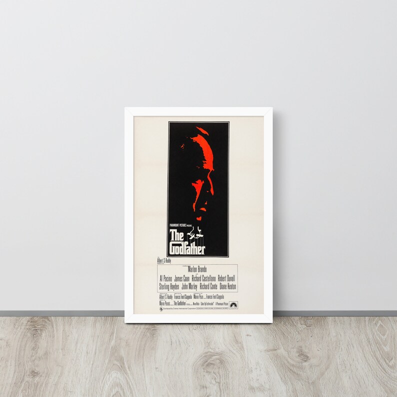 May include: A vintage movie poster for the film "The Godfather" featuring a red silhouette of Marlon Brando's face. The poster includes the film's title, director, and cast.