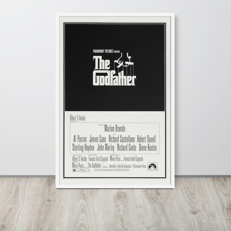 May include: A black and white movie poster for the film "The Godfather" featuring the title in a bold white font and a silhouette of a hand holding strings with puppets. The poster also includes the names of the actors and director.
