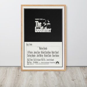 May include: A black and white movie poster for the film "The Godfather." The poster features the title in large white letters and a silhouette of a hand holding strings attached to a puppet. The cast includes Marlon Brando, Al Pacino, James Caan, and Robert Duvall.
