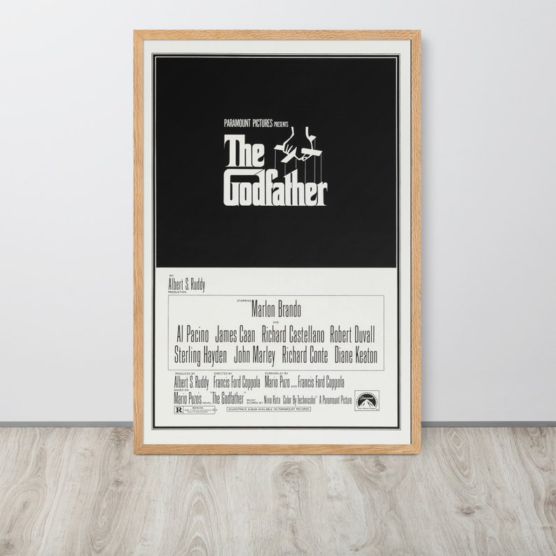 May include: A black and white movie poster for the film "The Godfather." The poster features the title in large white letters and a silhouette of a hand holding strings attached to a puppet. The cast includes Marlon Brando, Al Pacino, James Caan, and Robert Duvall.